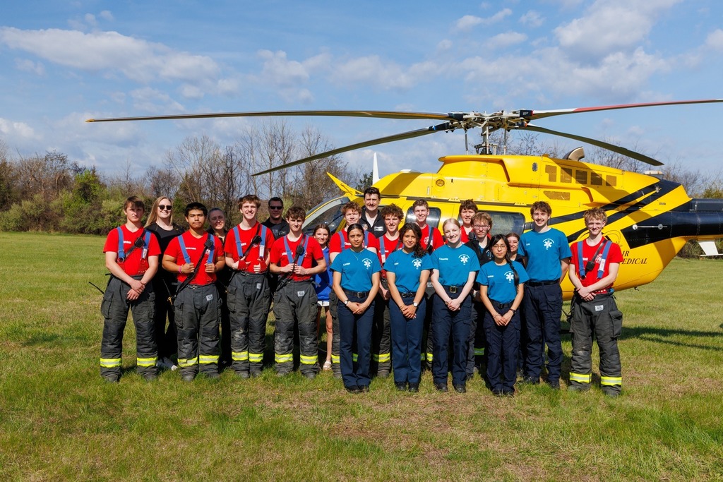 CTEC EMT and Firefighter students pose in front of the AirCare 6 medical helicopter on a grassy field, wearing program uniforms during a special visit from the flight crew.