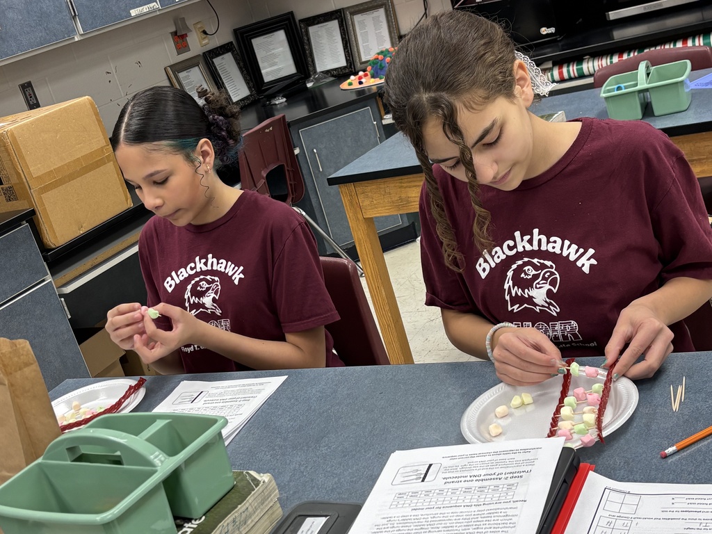 Two students sit at a classroom table assembling DNA models using candy and toothpicks, following a worksheet as part of a hands-on science activity.