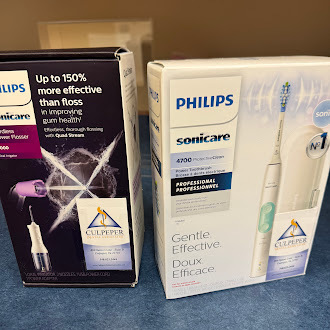 Two boxed Philips Sonicare dental‑care products displayed on a blue surface. The box on the left is a Philips Sonicare AirFloss Pro, shown with an image of the device spraying between teeth and a small Culpeper Family Dentistry logo. The box on the right is a Philips Sonicare 4700 Professional electric toothbrush, pictured with the toothbrush and replacement brush heads.
