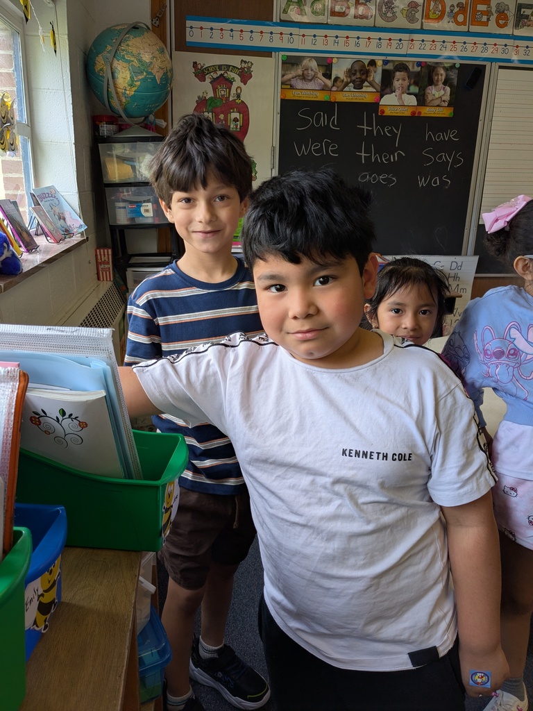 Several students stand together near a classroom bookshelf, looking toward the camera with relaxed expressions.