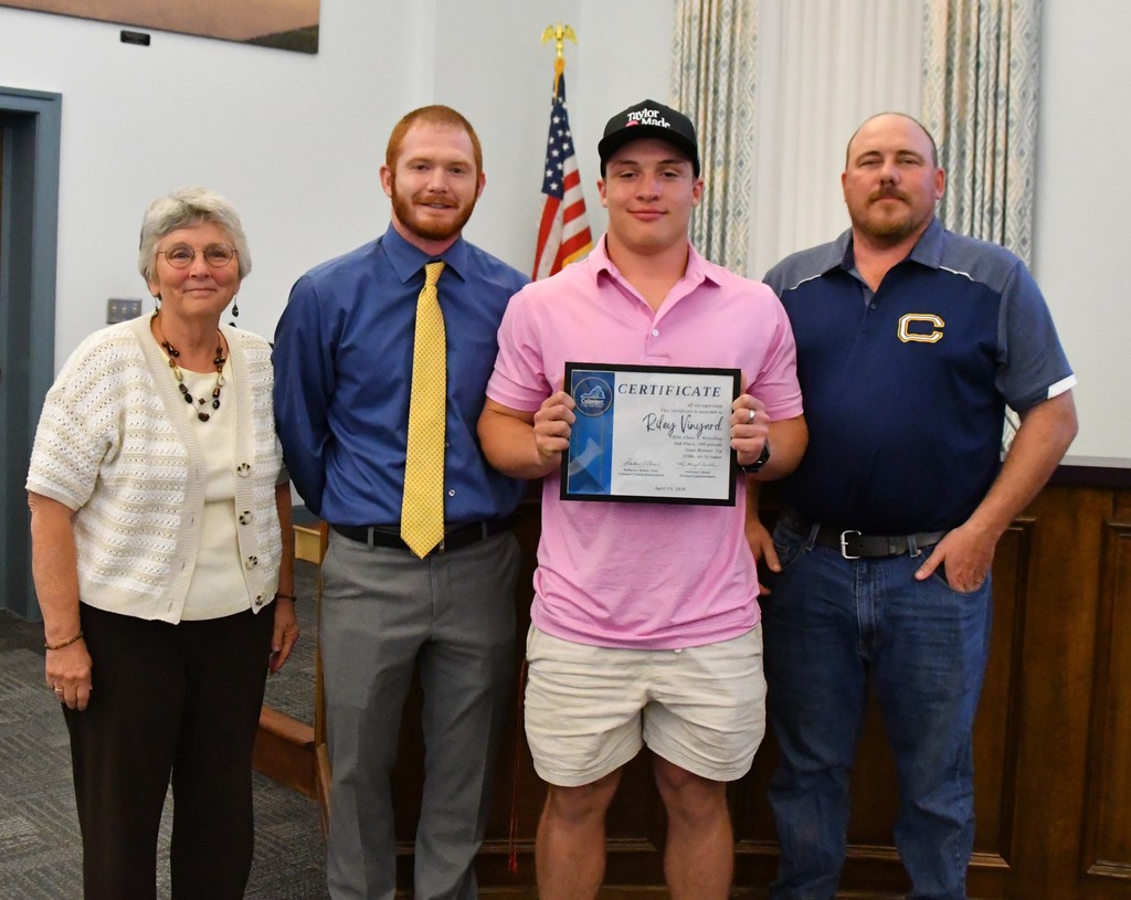 student holding certificate with coaches and board member in board room