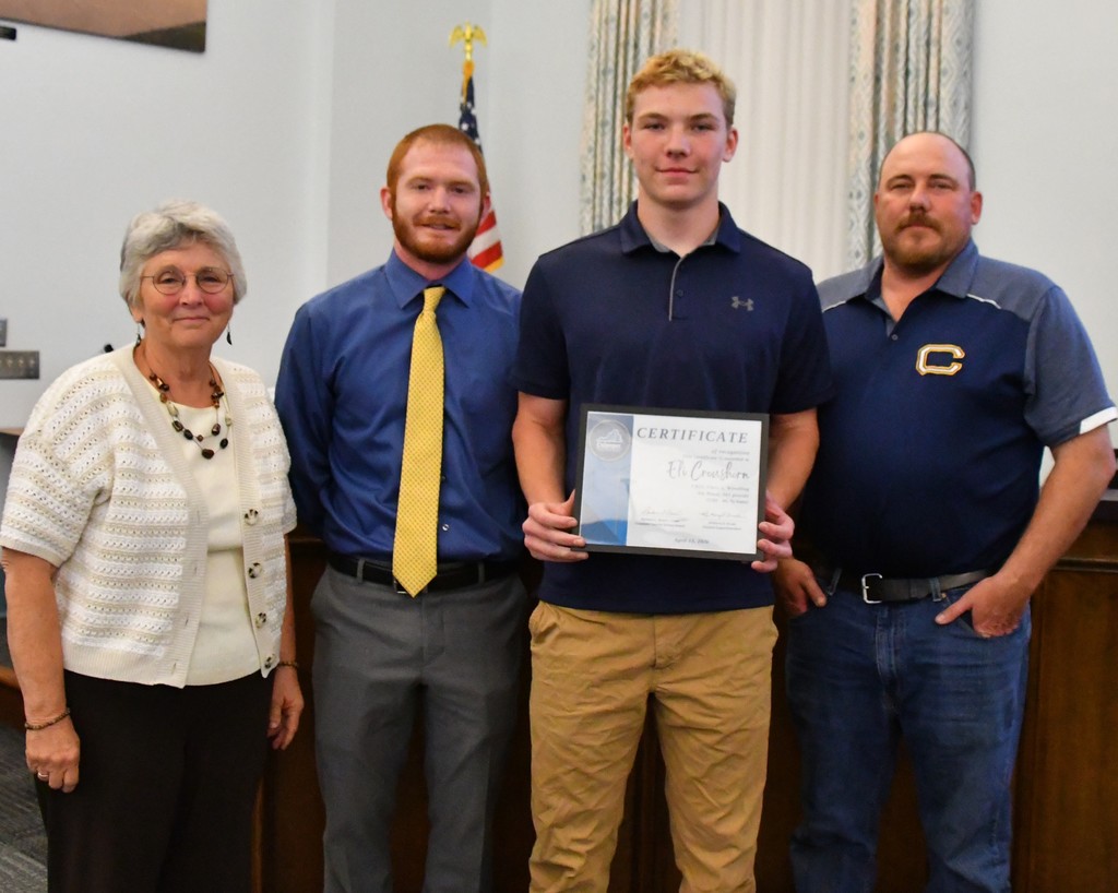 student holding certificate with coaches and board member in board room