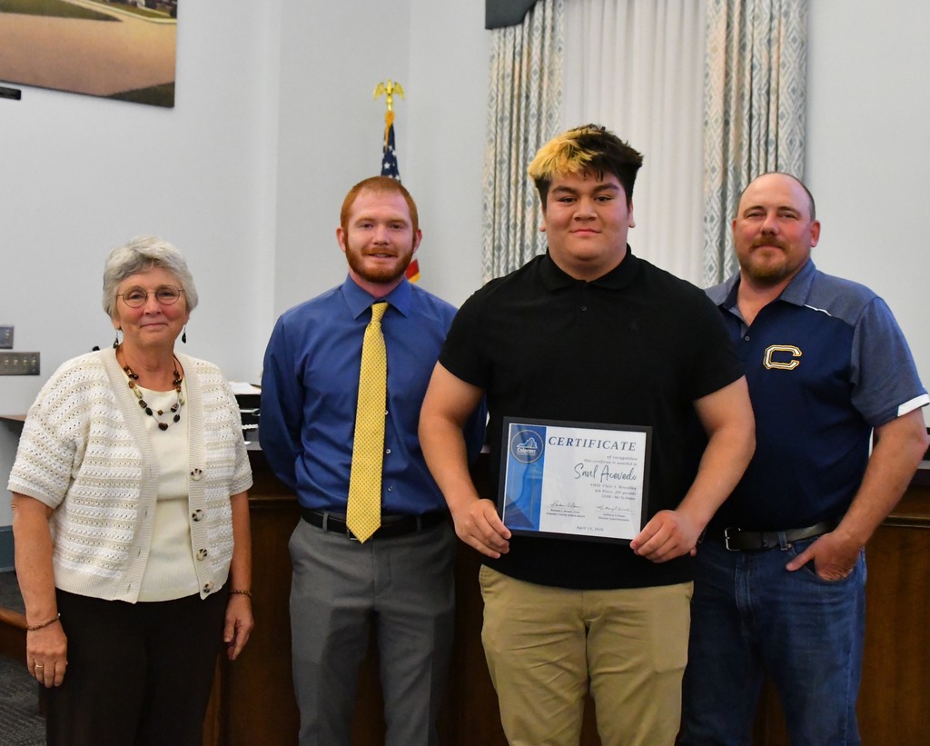 student holding certificate with coaches and board member in board room