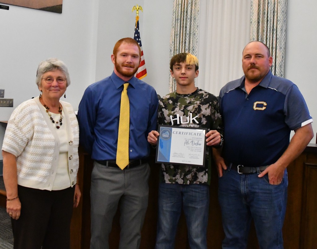 student holding certificate with coaches and board member in board room