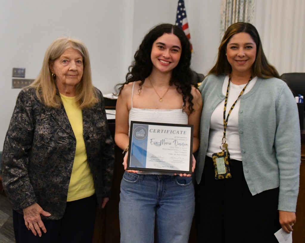 student holding certificate in board room with teacher and board member