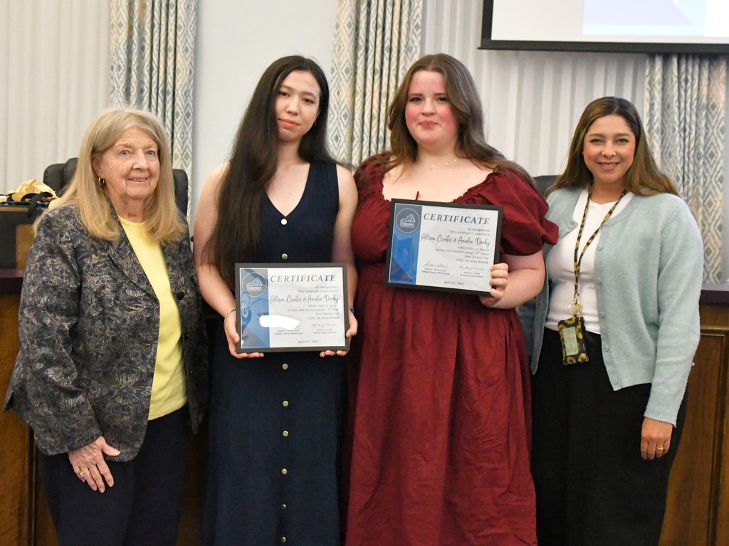 students holding certificates in board room with teacher and board member