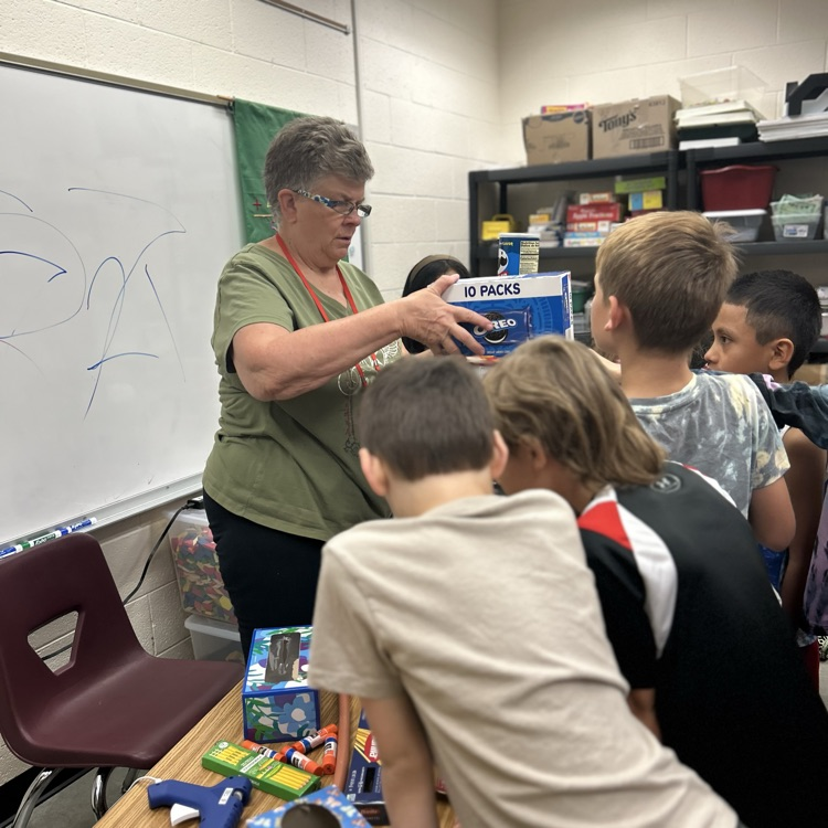 teacher standing and helping a group of students stack boxes