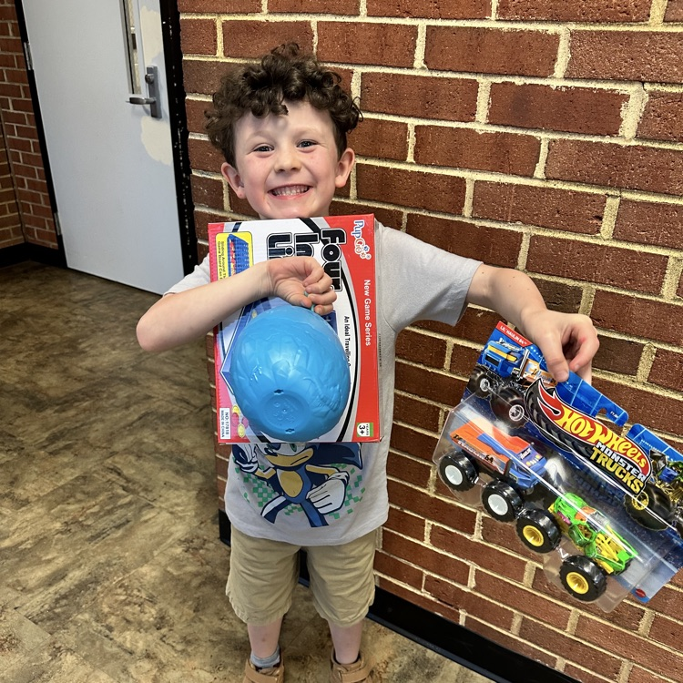     A young boy grins while holding up two prizes—a game and a toy truck—after winning at bingo.