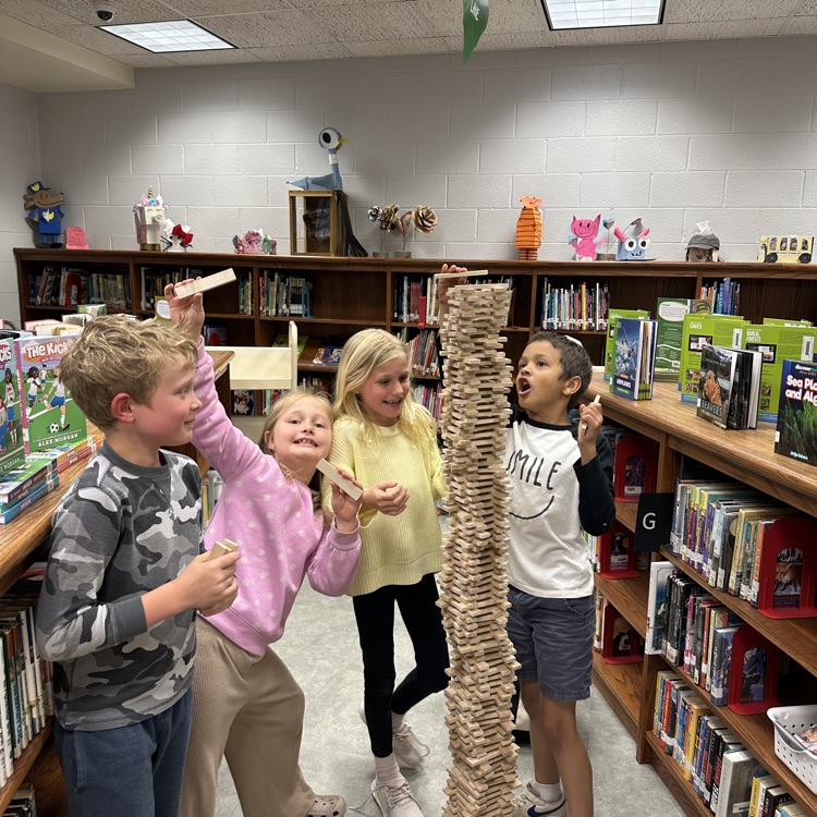 students pictured standing around a stack of keva planks taller themselves 