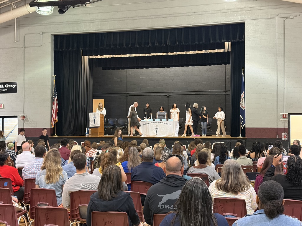 Wide view of a school auditorium filled with families and students watching a National Junior Honor Society induction ceremony taking place on stage.