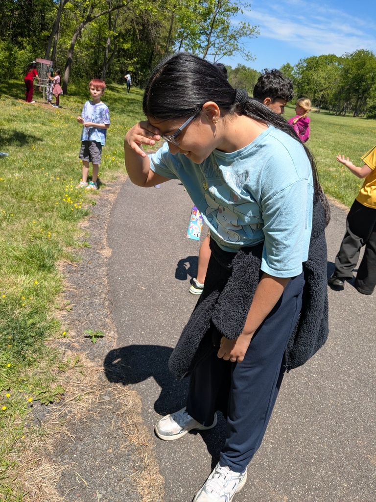 Students stand on a paved path outdoors, one student shielding their eyes from the sun while others explore the area.