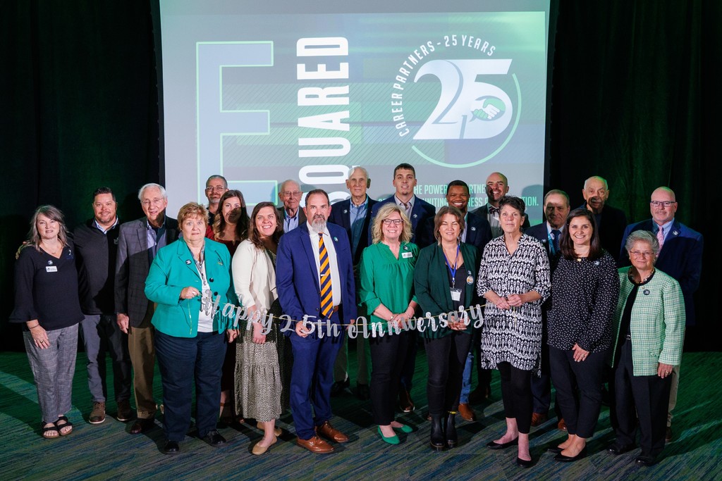 A large group of community members and school partners pose together on a stage in front of a screen displaying “Career Partners – 25 Years.” The group includes men and women dressed in business and business-casual attire, standing shoulder to shoulder and smiling at the camera. The stage is lit with green accent lighting, and a decorative “Happy 25th Anniversary” sign is visible in front of the group, celebrating the long-standing partnership supporting Culpeper County Public Schools.