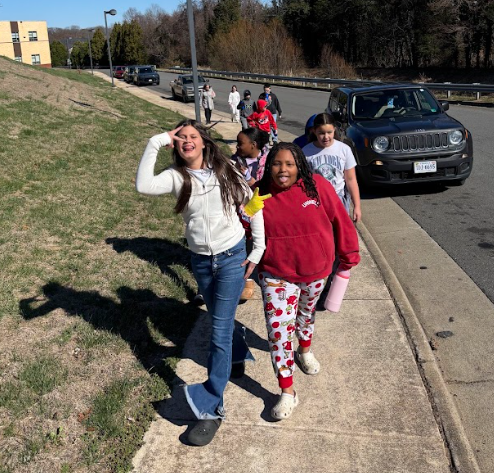 Children walking on a sidewalk, one with a white jacket and another in a red jacket.