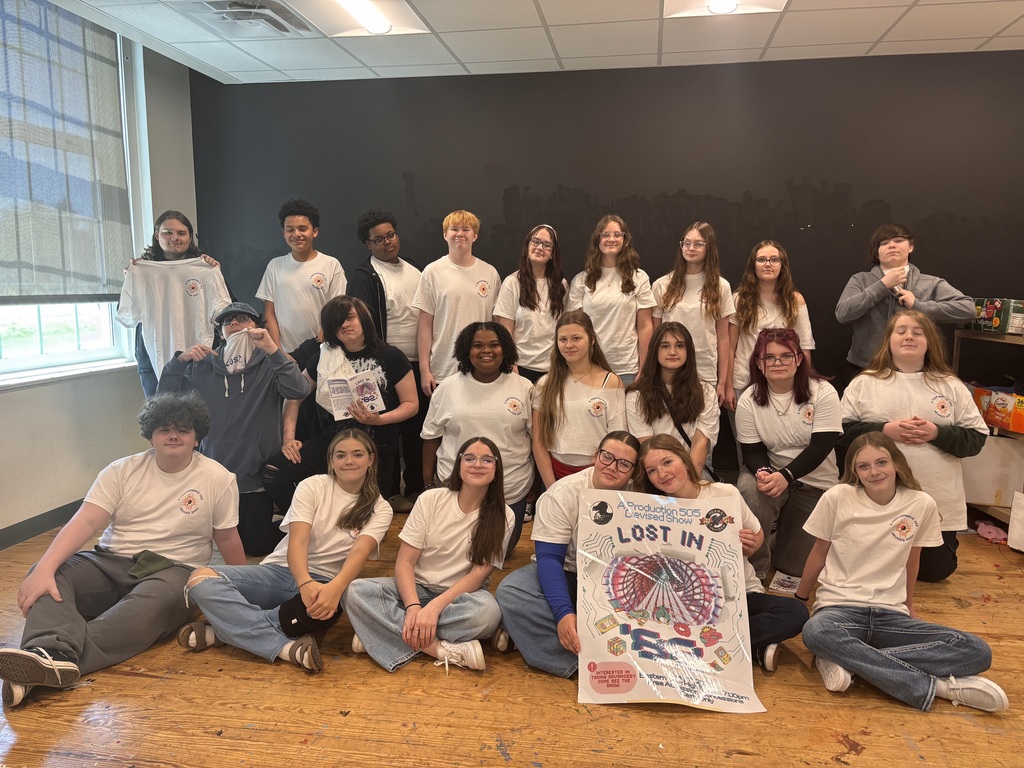 A group of people in white shirts poses for a photo in a room with a dark wall.