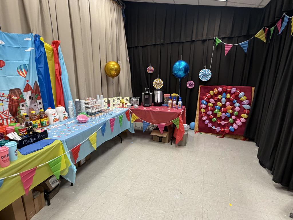 Room with tables covered in colorful tablecloths and decorations, including balloons, banners, and a dartboard.