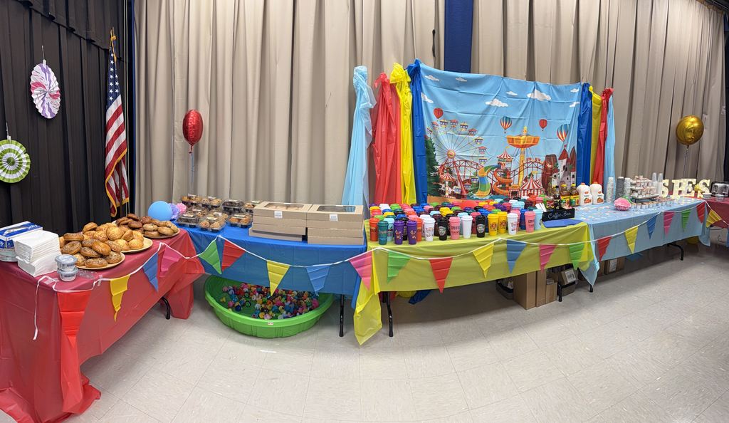 Tables set up with colorful tablecloths, food, and party items in a room with a flag.