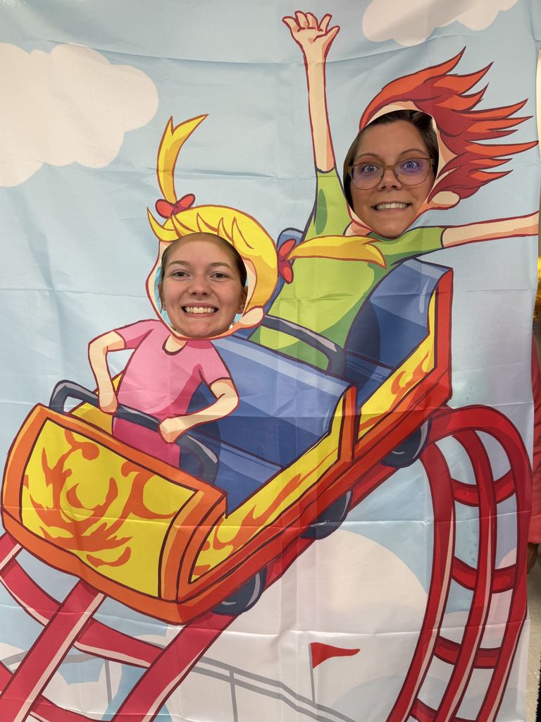 Two children in a photo booth cutout with a roller coaster. One has red hair and glasses, and the other has blonde hair.