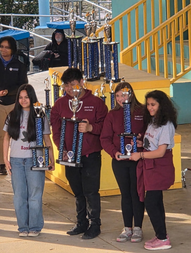 Five individuals stand on a sidewalk, holding trophies. They are smiling and posing for a photo.