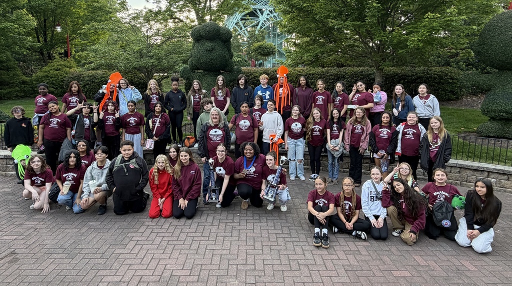 A group of people, some in maroon shirts, are posing for a photo in an outdoor park.