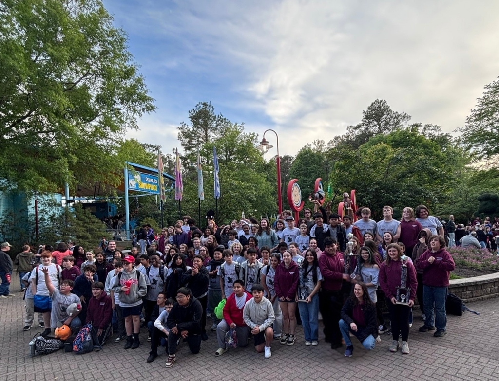A large group of people in maroon and white shirts poses for a photo in a park.