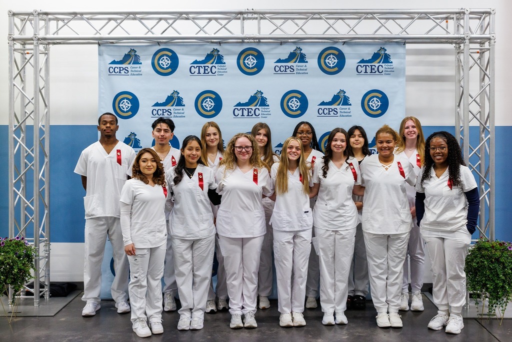 A group of medical students in white uniforms, stands in front of a blue backdrop with text.