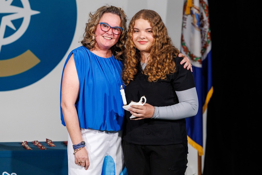 Two women, one in blue and the other in black, stand next to a table with a candle.