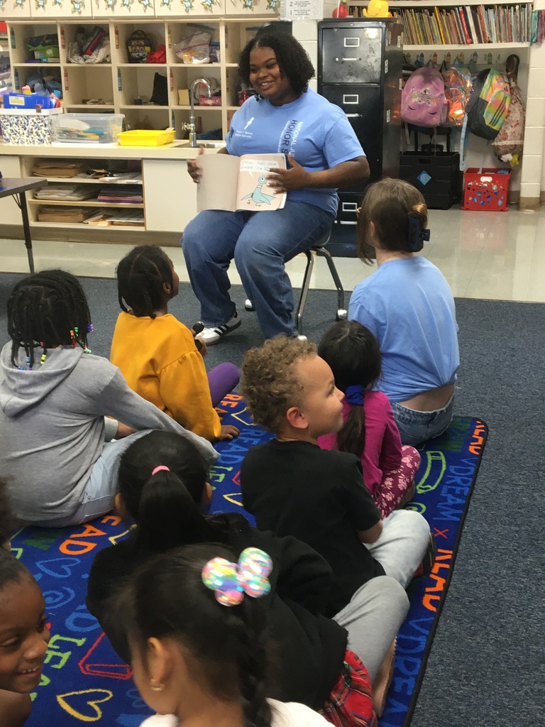A teacher reads a book to a group of children sitting on the floor in a classroom.