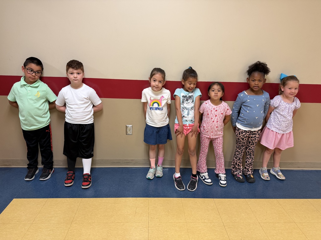 six preschool aged students stand against a classroom wall and pose for a picture in their mismatched outfits for M day