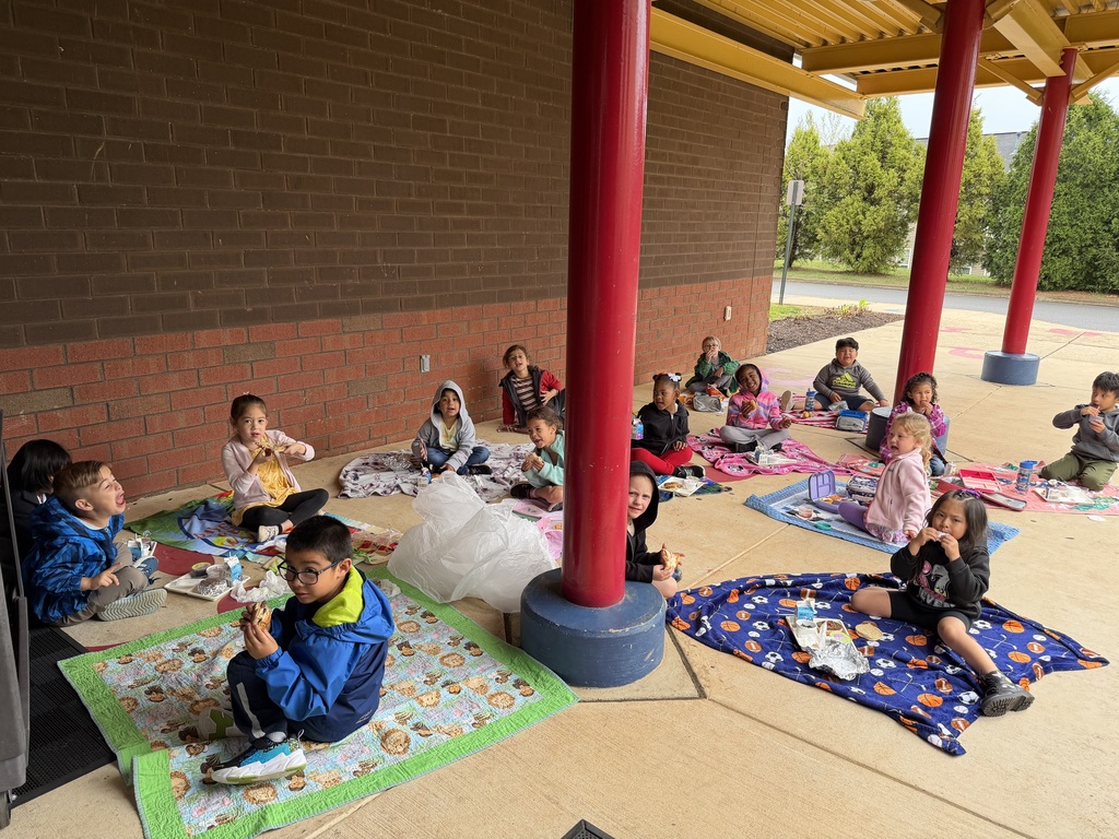 a group of preschool aged students sit on blankets outside of the school and have a picnic lunch