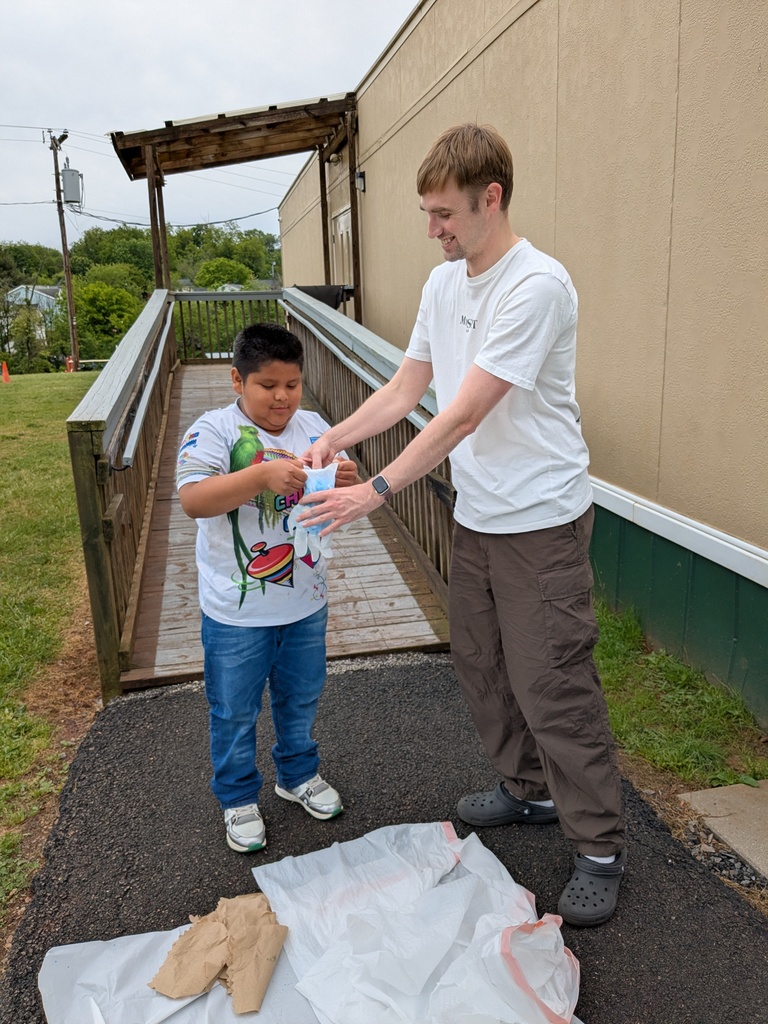 A man in a white shirt helps a child in a yellow shirt pour liquid into a container.