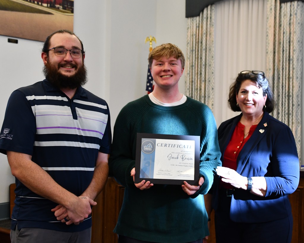 Three people standing together holding a certificate. Man in striped shirt, man in green sweater, woman in blue jacket.