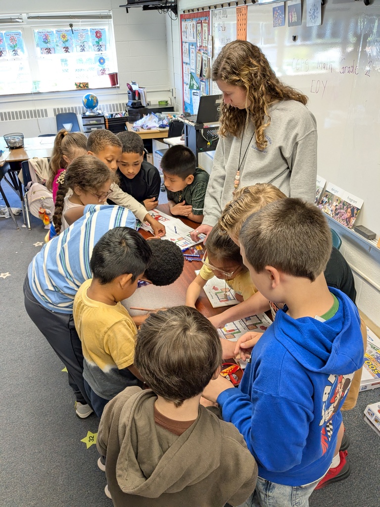 A classroom with children and an adult, gathered around a table with materials, engaged in a project.