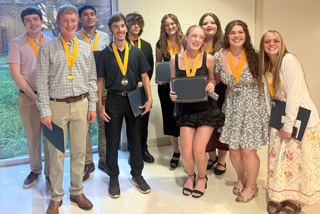 A group of young people stands together, holding medals and certificates, smiling for a photo.