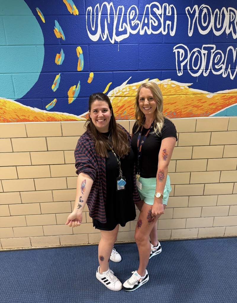 Two women standing in front of a blue wall with "Unleash Your Potential" written on it.