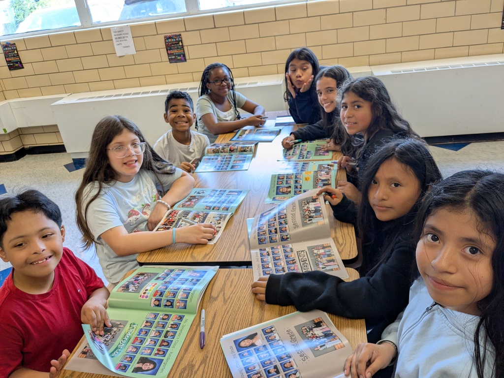 A classroom with children seated around a table with books. They appear to be smiling and engaged.