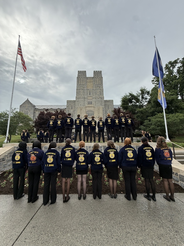 A group of people in blue jackets with numbers stand in front of a university building.