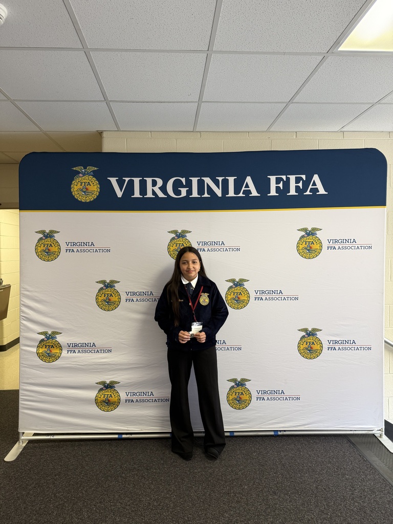Person in black holding a trophy stands in front of a Virginia FFA banner with yellow logos.