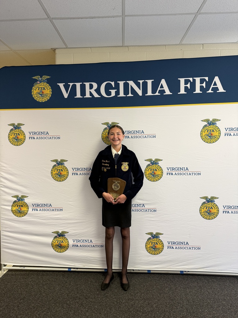 A person stands with an award in front of a white backdrop with logos and the words "VIRGINIA FFA."
