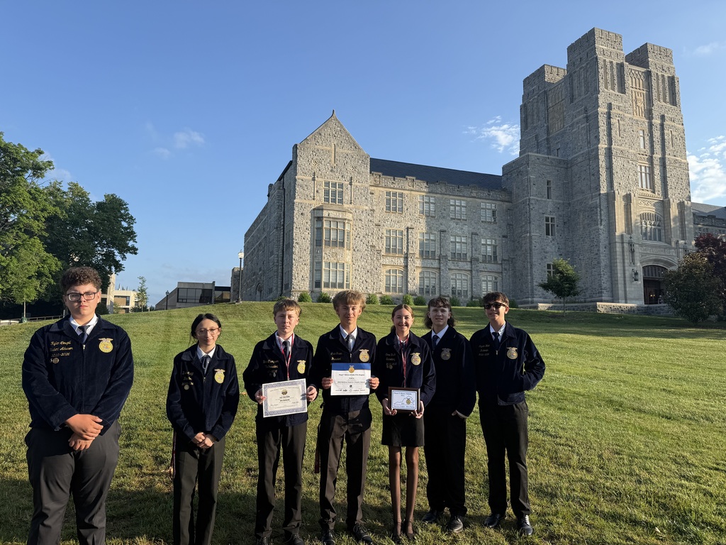 Seven individuals in matching uniforms hold certificates in front of a large stone building with a clear sky.