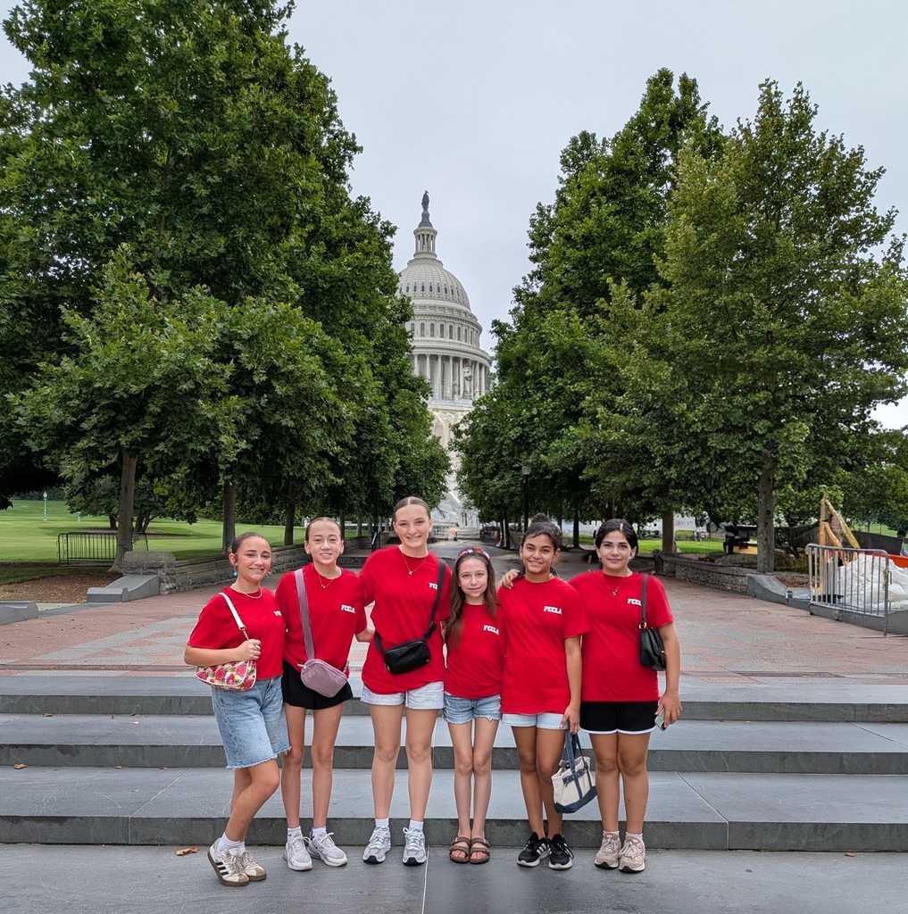 Six Culpeper Middle School FCCLA students stand together on the steps in front of the U.S. Capitol in Washington, D.C., during the FCCLA National Leadership Conference. The students are wearing matching red FCCLA T-shirts with casual shorts and sneakers, smiling for the camera with the Capitol dome centered in the background and framed by large green trees on both sides.