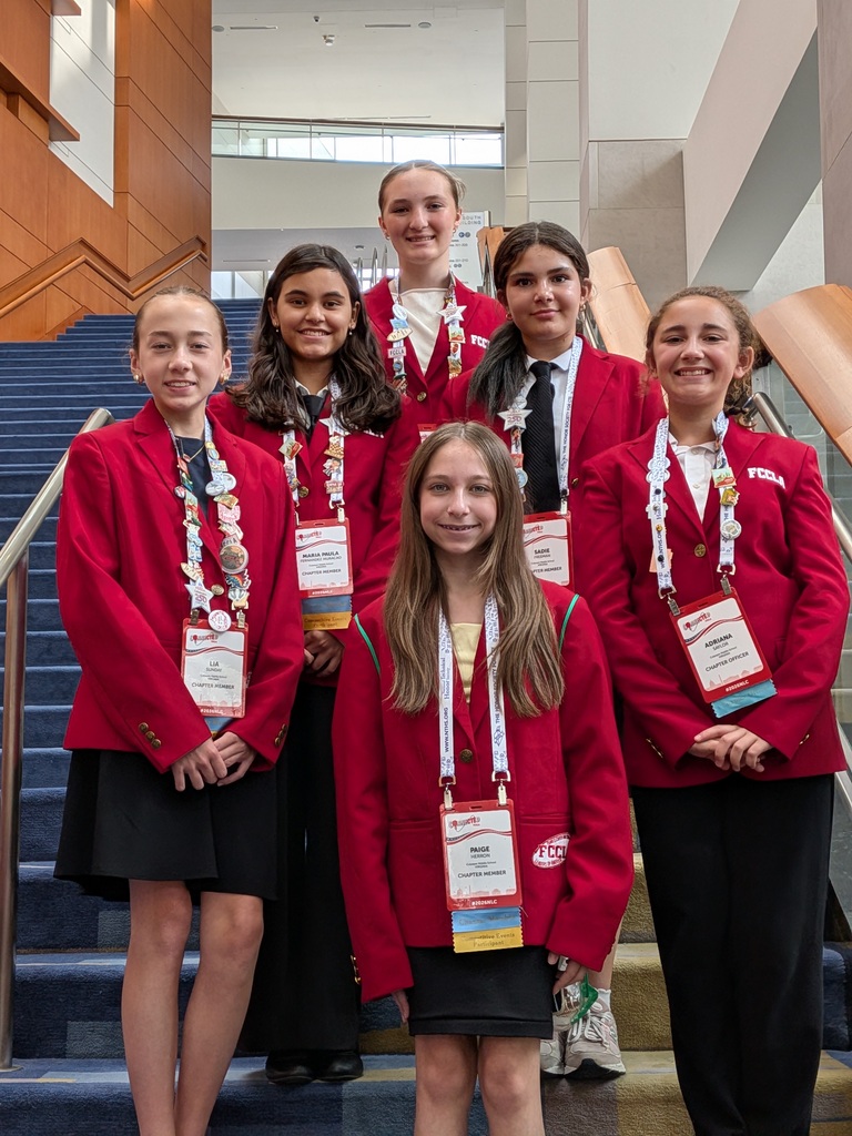 Six Culpeper Middle School FCCLA students pose inside the Washington Convention Center during the FCCLA National Leadership Conference. The students are wearing official red FCCLA blazers over professional attire, displaying conference name badges and award ribbons around their necks. They are standing on a staircase, smiling proudly after representing Virginia at the national conference.