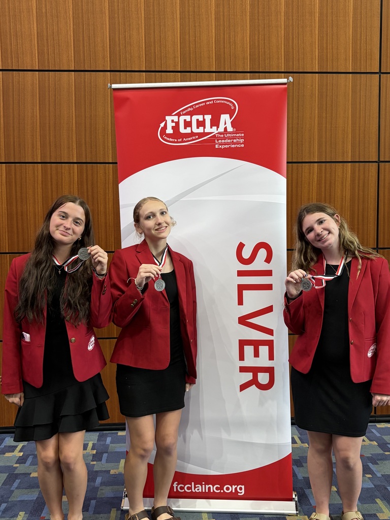 Three women stand next to each other, holding medals. They wear red blazers and black dresses. A banner behind them reads "FCCLA SILVER."