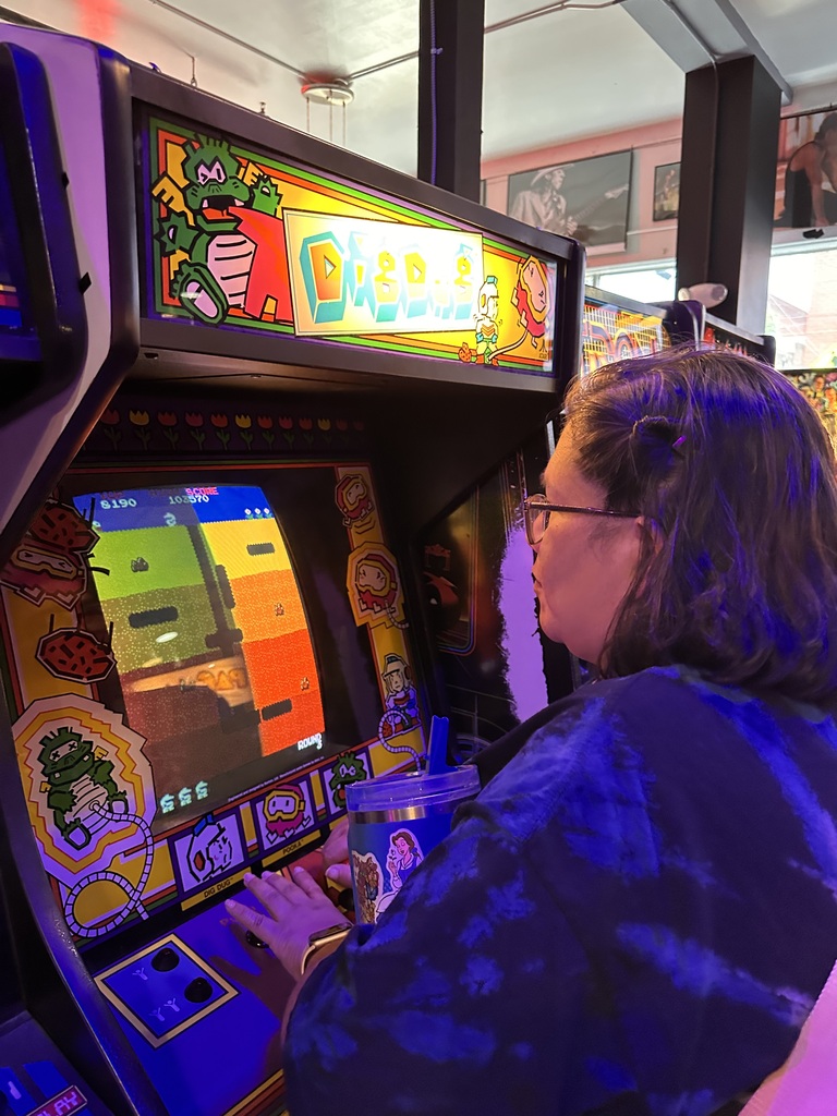 Person with glasses plays an arcade game featuring a digital screen with a frog character.