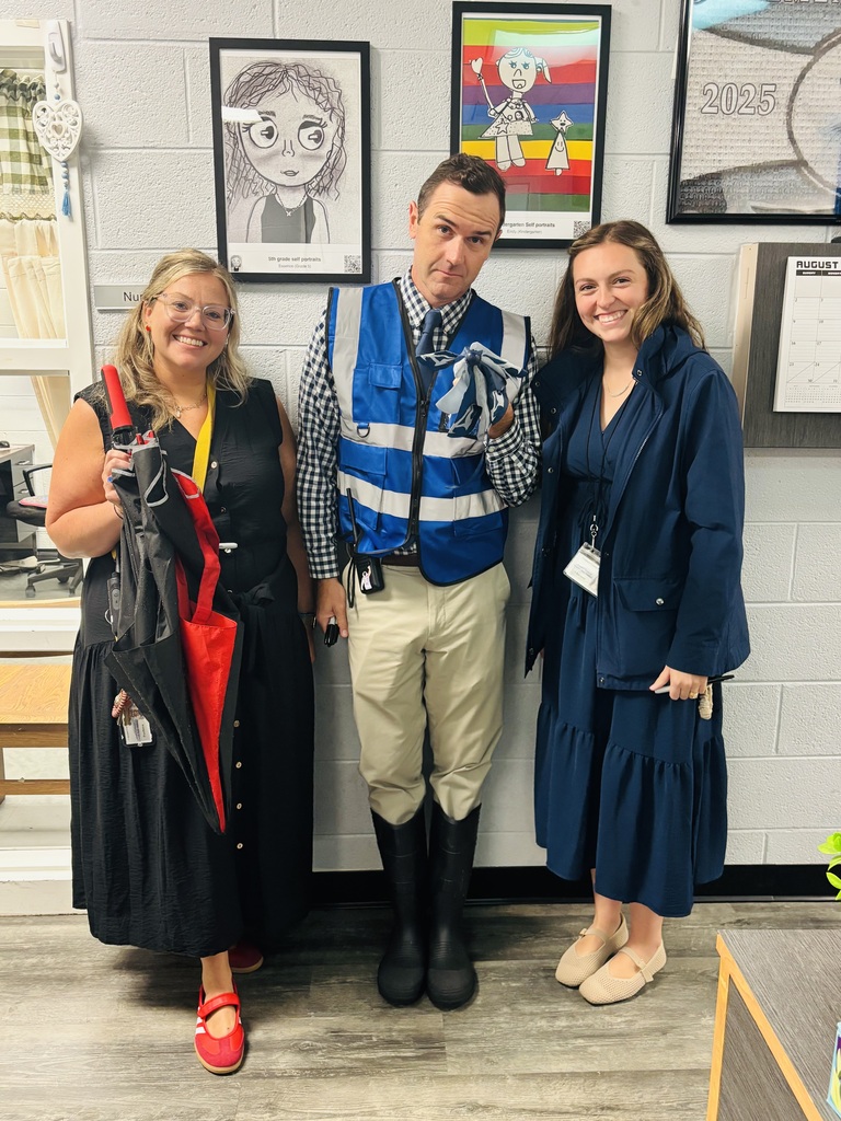 Three adults in costumes stand together in a room with white walls and wooden floors. They are next to framed artwork.