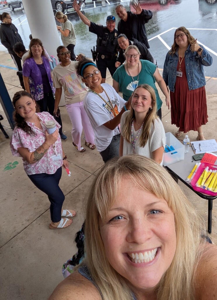 A selfie taking outside of the school building in the rain of smiling staff as they wait for the buses to arrive.
