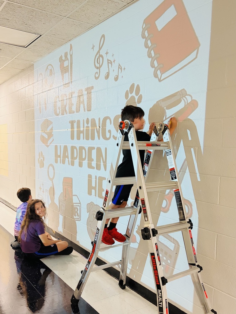 Children seated on floor and one on a ladder sketching a mural onto a wall