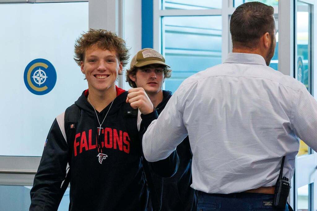A student wearing a Falcons hoodie smiles and gives a fist bump while entering the Culpeper Technical Education Center, as another student follows behind and a staff member greets students at the entrance.