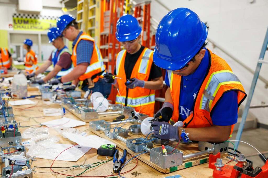 lectricity students put their wiring skills into practice during a hands-on lab, assembling electrical circuits while following industry safety standards with hard hats, safety glasses, gloves, and high-visibility vests.