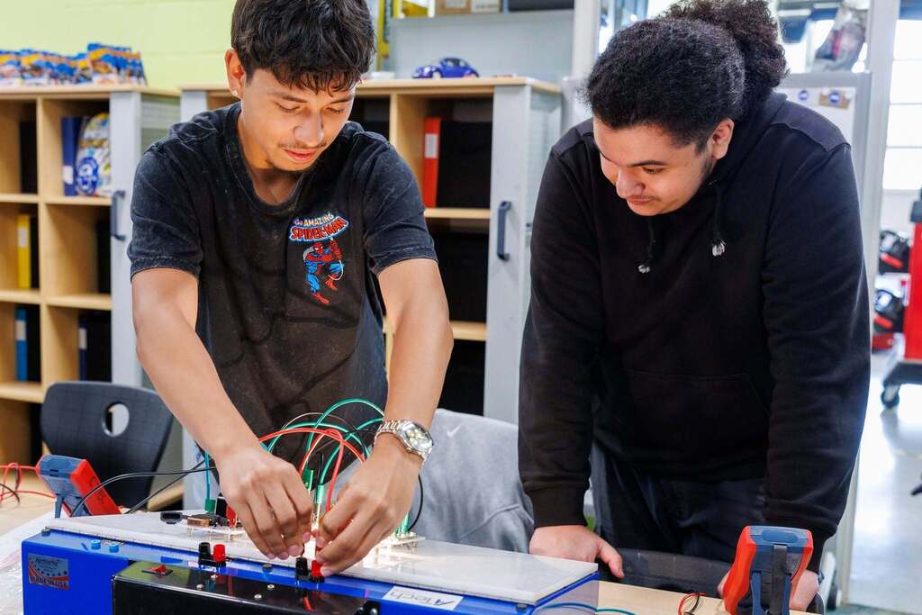 Two students work together in the Automotive Technology lab, with one student connecting wires on an automotive electrical training board while the other observes and assists during a hands-on diagnostic and electrical systems lesson.