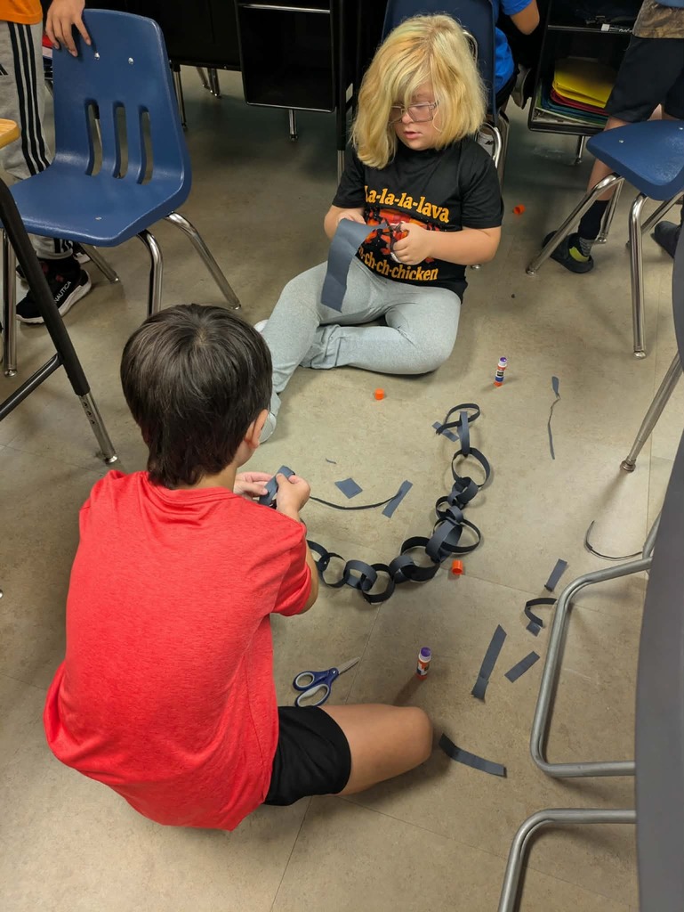 Children sitting on the floor, one using scissors to cut tape while the other holds a strip.